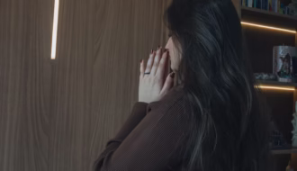 A woman prays in a serene room with an illuminated cross and open Bible.