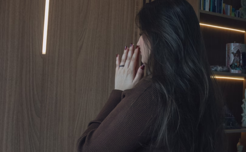 A woman prays in a serene room with an illuminated cross and open Bible.